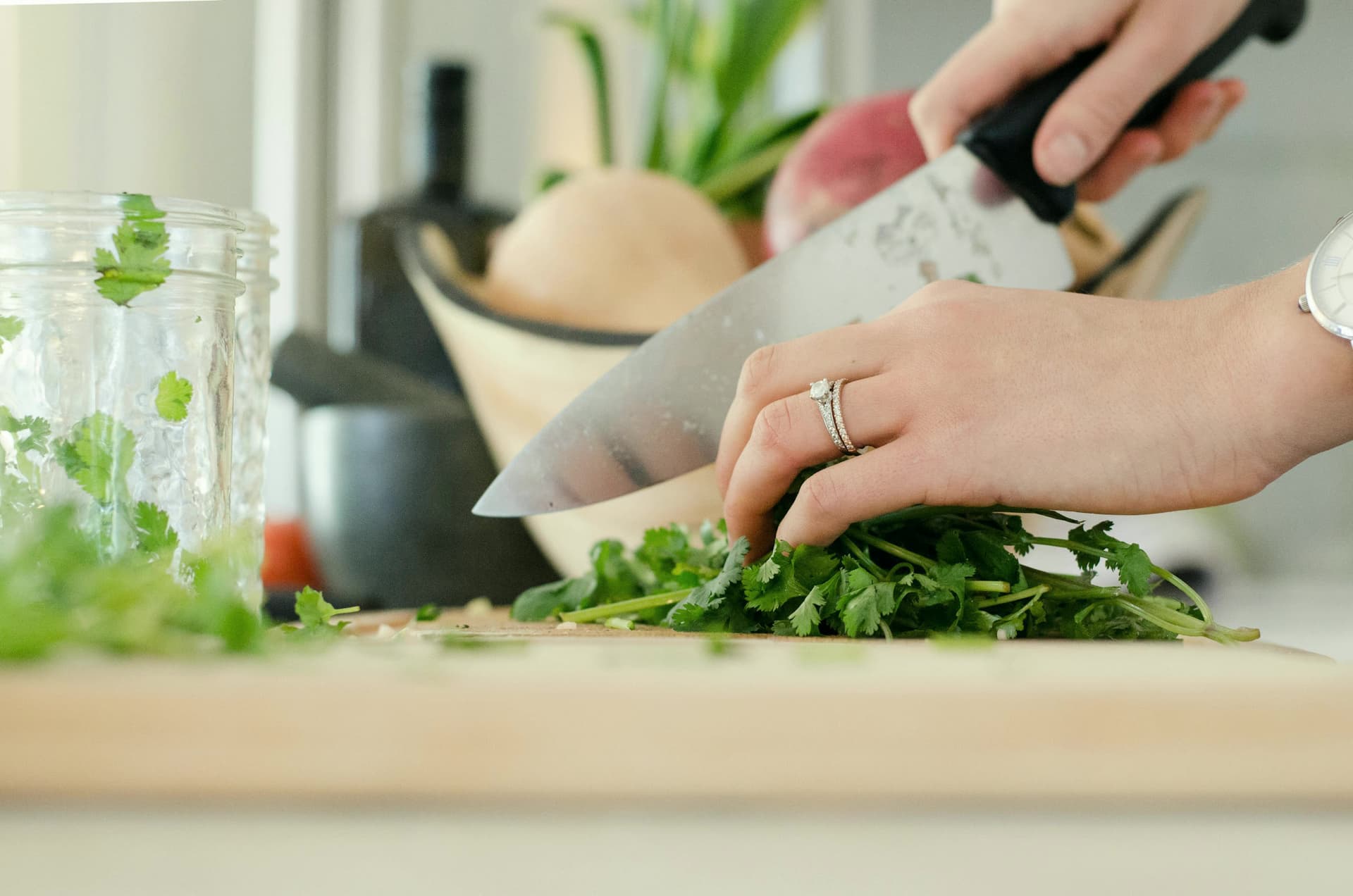 Hands chopping fresh herbs on a wooden board in a bright kitchen.