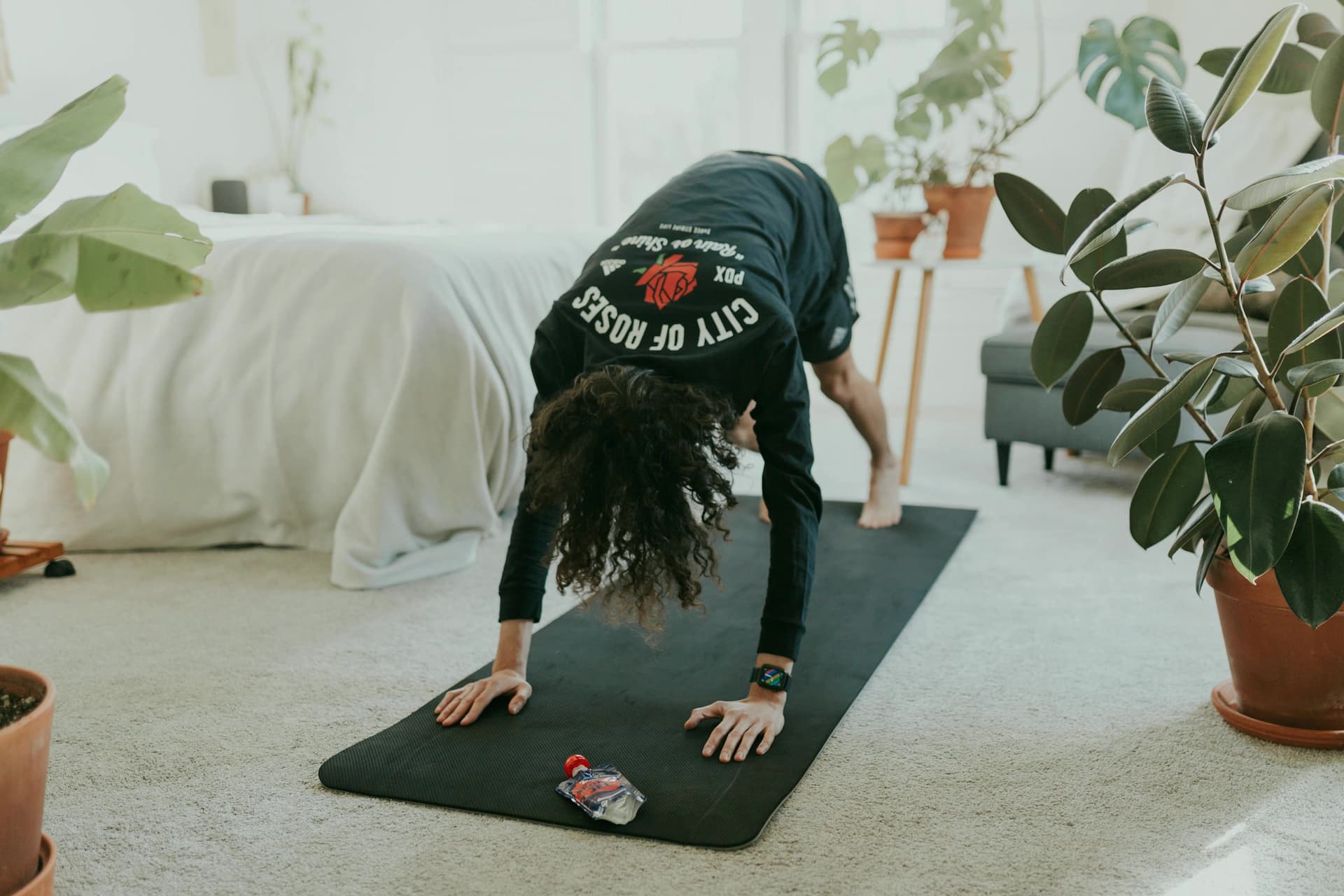 A woman in a bright bedroom holding a downward dog on a yoga mat.